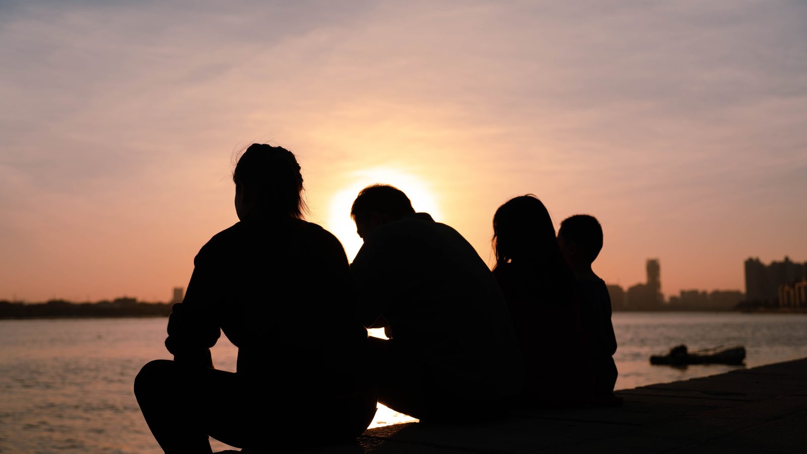 A family sitting together at the water's edge at sunset